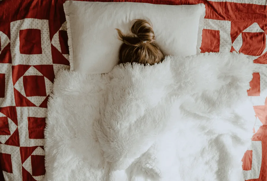 Girl under white fur textile covers.