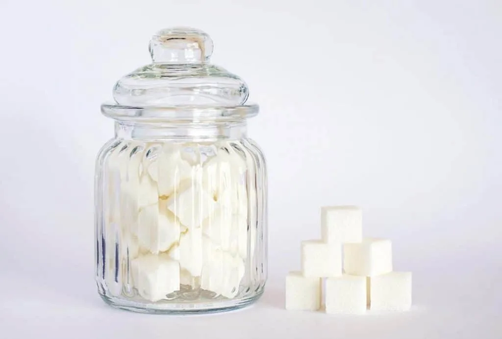 A jar full of sugar with some sugar cubes off to the side.