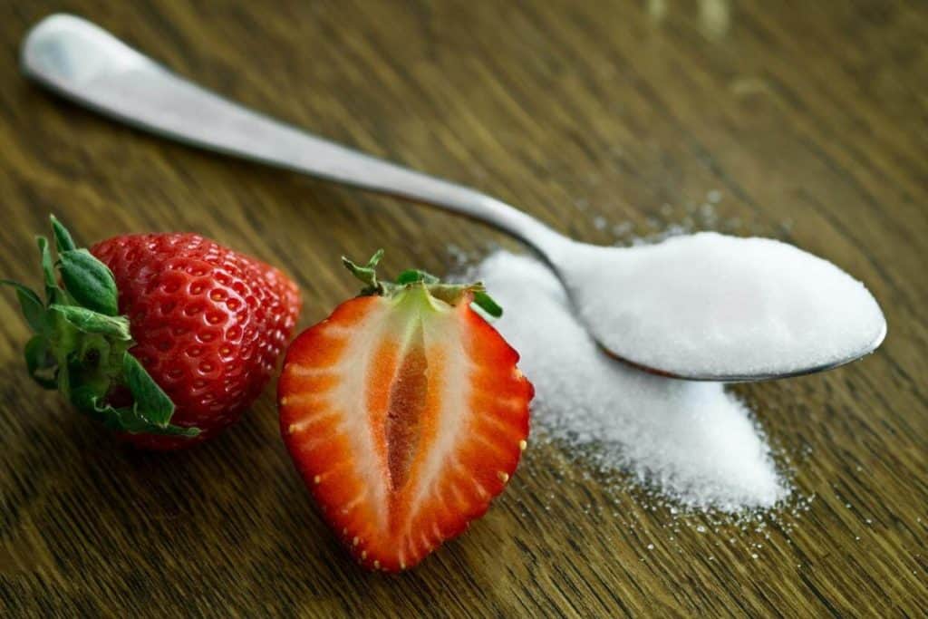 A picture of a spoonful of sugar with two strawberries beside it

