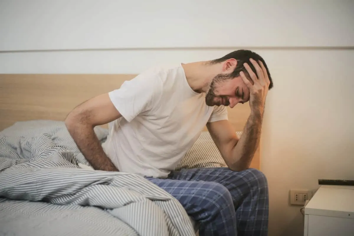 Man having a headache sitting on his bed