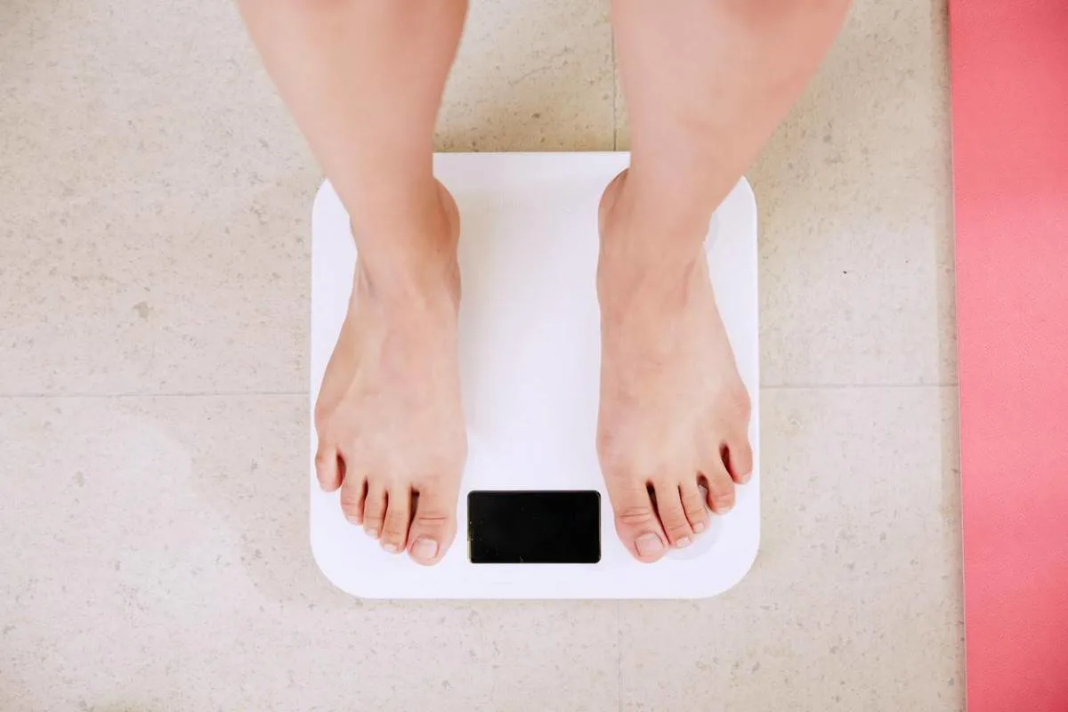 Person measuring his weight on weighing scale