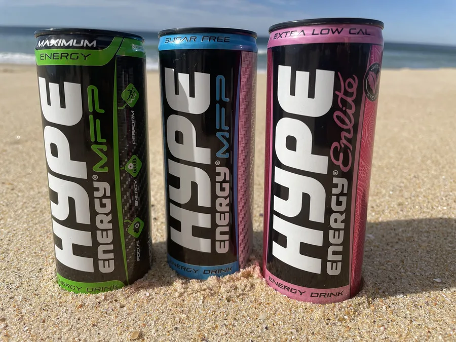 3 different flavored cans of Hype energy drink placed on a beach