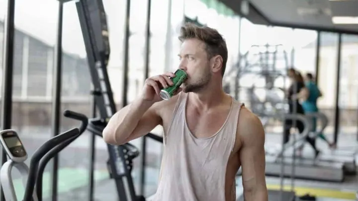 a man drinking an energy drink sitting in a gym