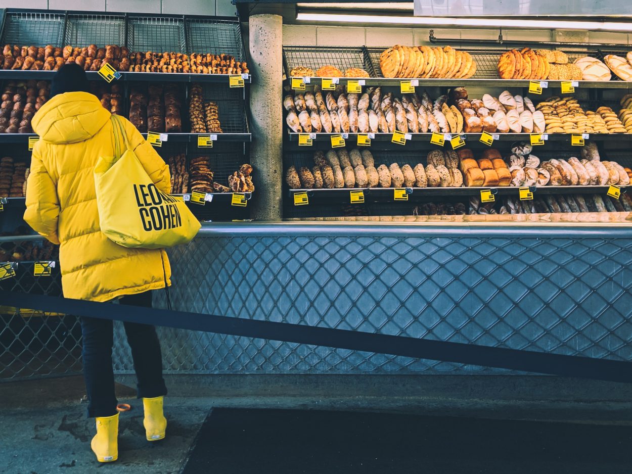 A person in yellow jacket and with yellow bag standing in a bread store