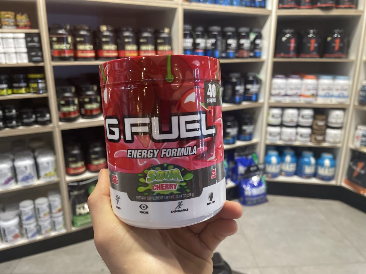 A person holding a tub of G Fuel in sour cherry flavor