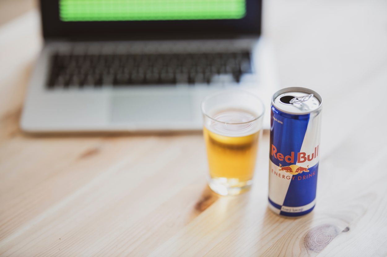 A can of Red Bull placed beside a glass and a laptop