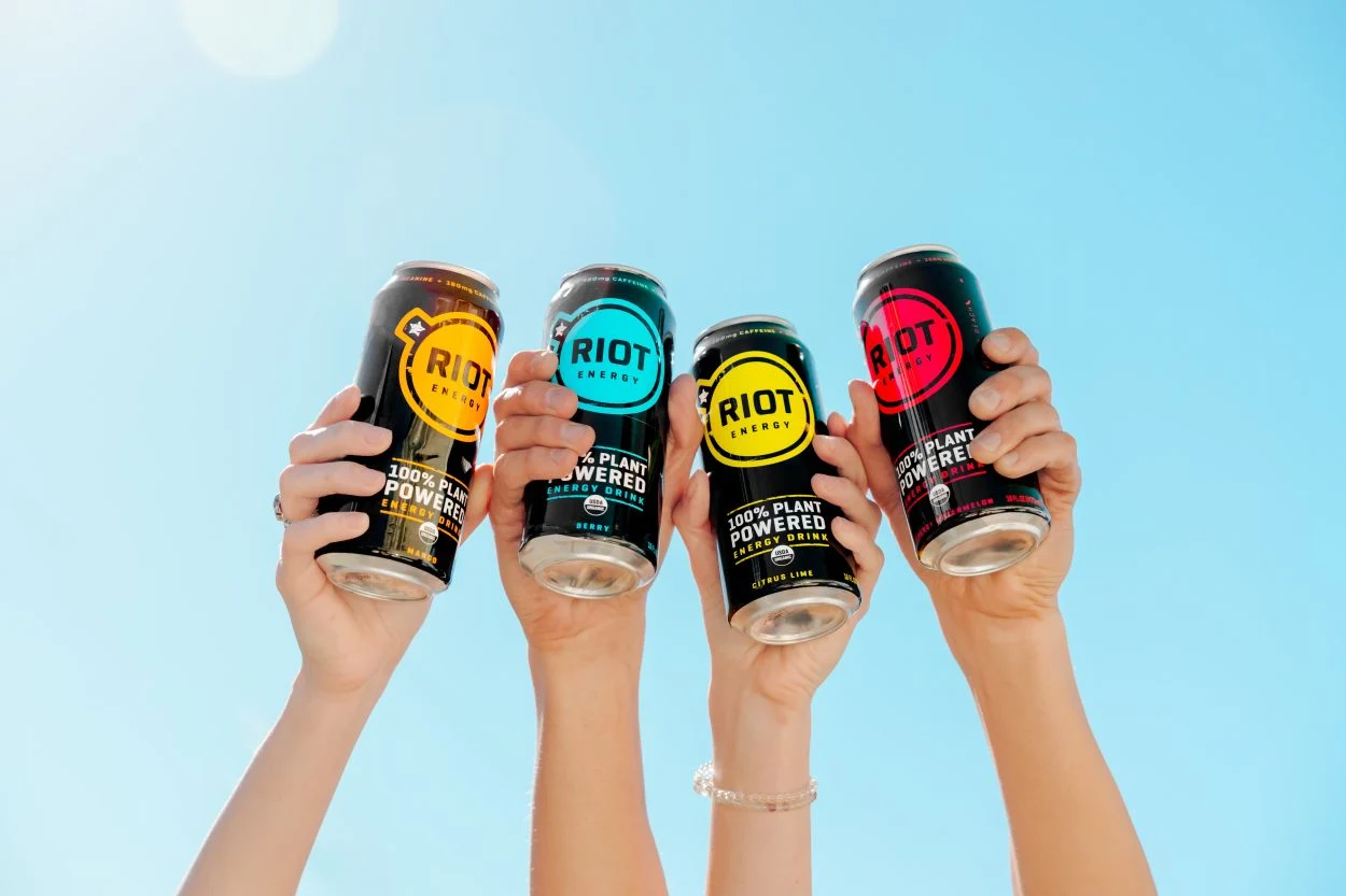 Four hands of people holding one can or Riot Energy drink