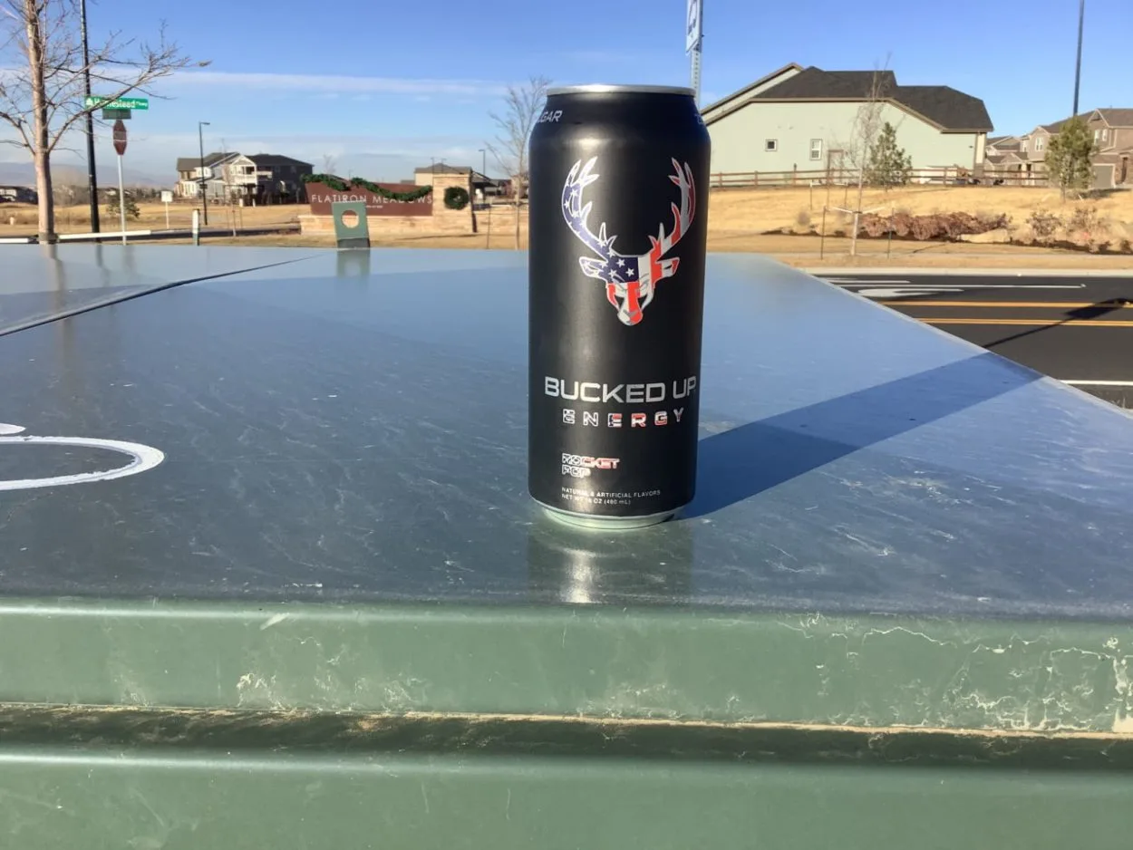 A can of Bucked Up placed on a surface with houses behind it
