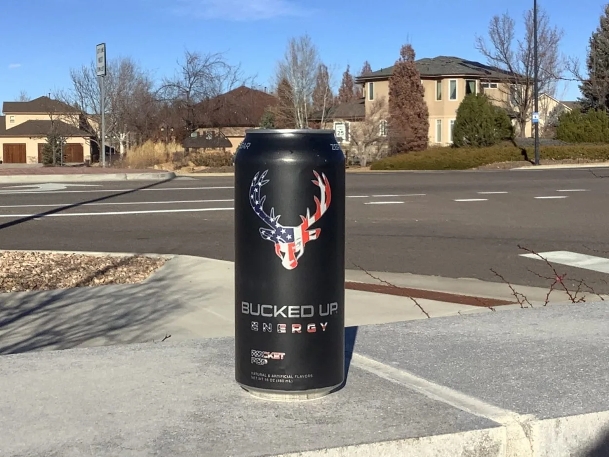 A can of Bucked Up placed on a surface with houses behind it