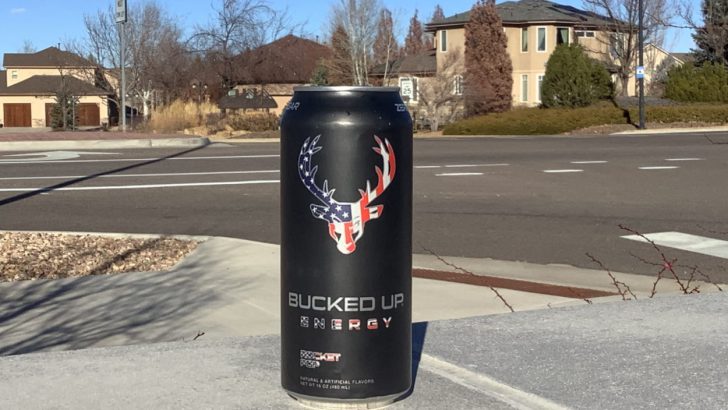 A can of Bucked Up energy drink placed on a surface with houses behind it