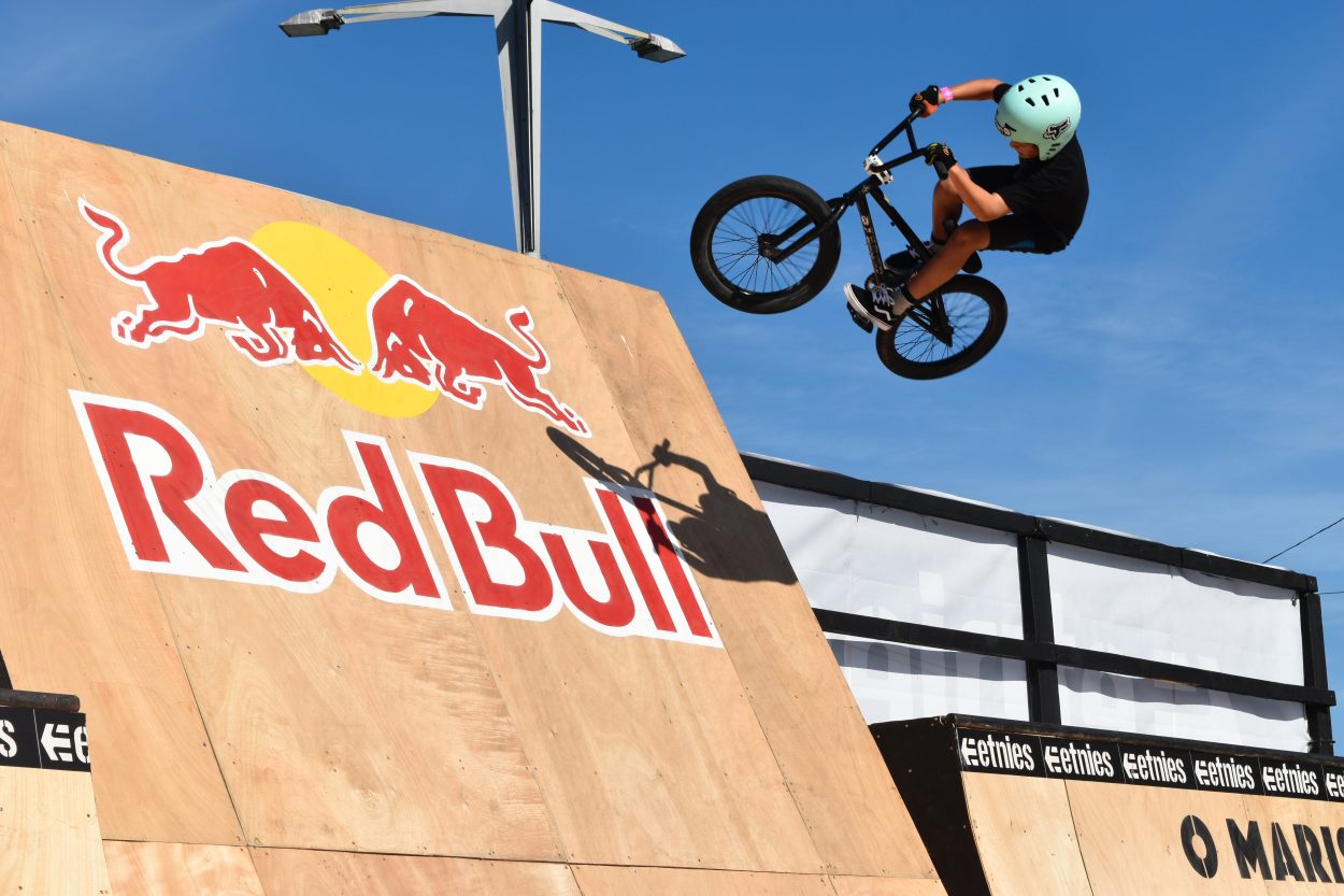 A person on a bicycle jumping above from a wooden board that has Red Bull logo on it