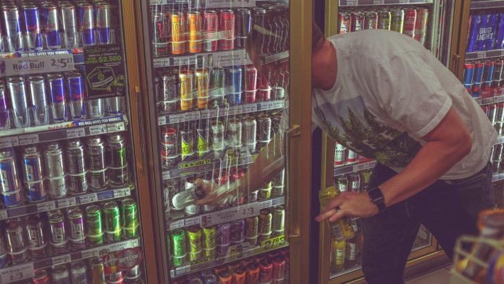 A man taking an energy drink from a freezer in astore
