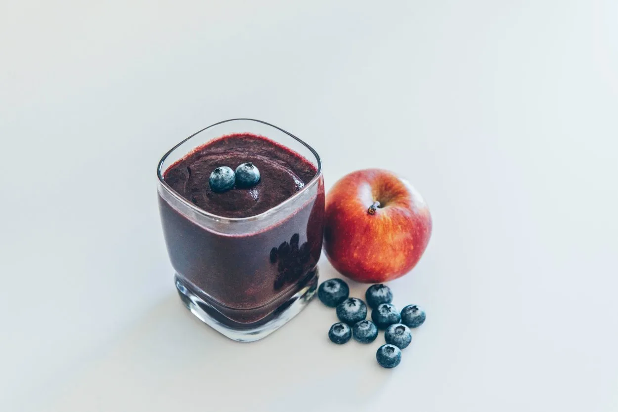 A glass of smoothy placed with an apple and some berries