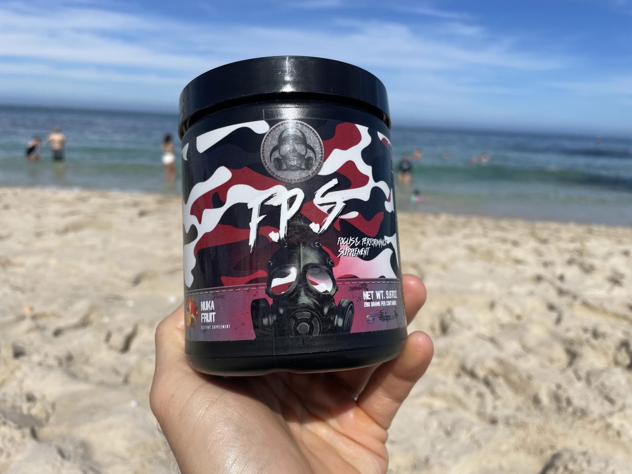 A person holding a tub of Outbreak Nutrition energy powder on a beach