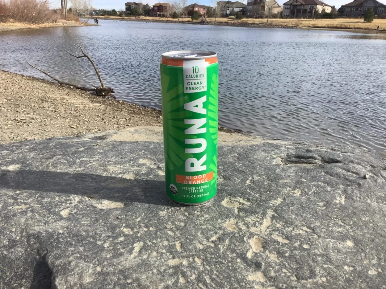 A can of RUNA Clean energy drink on the rock with a lake behind it