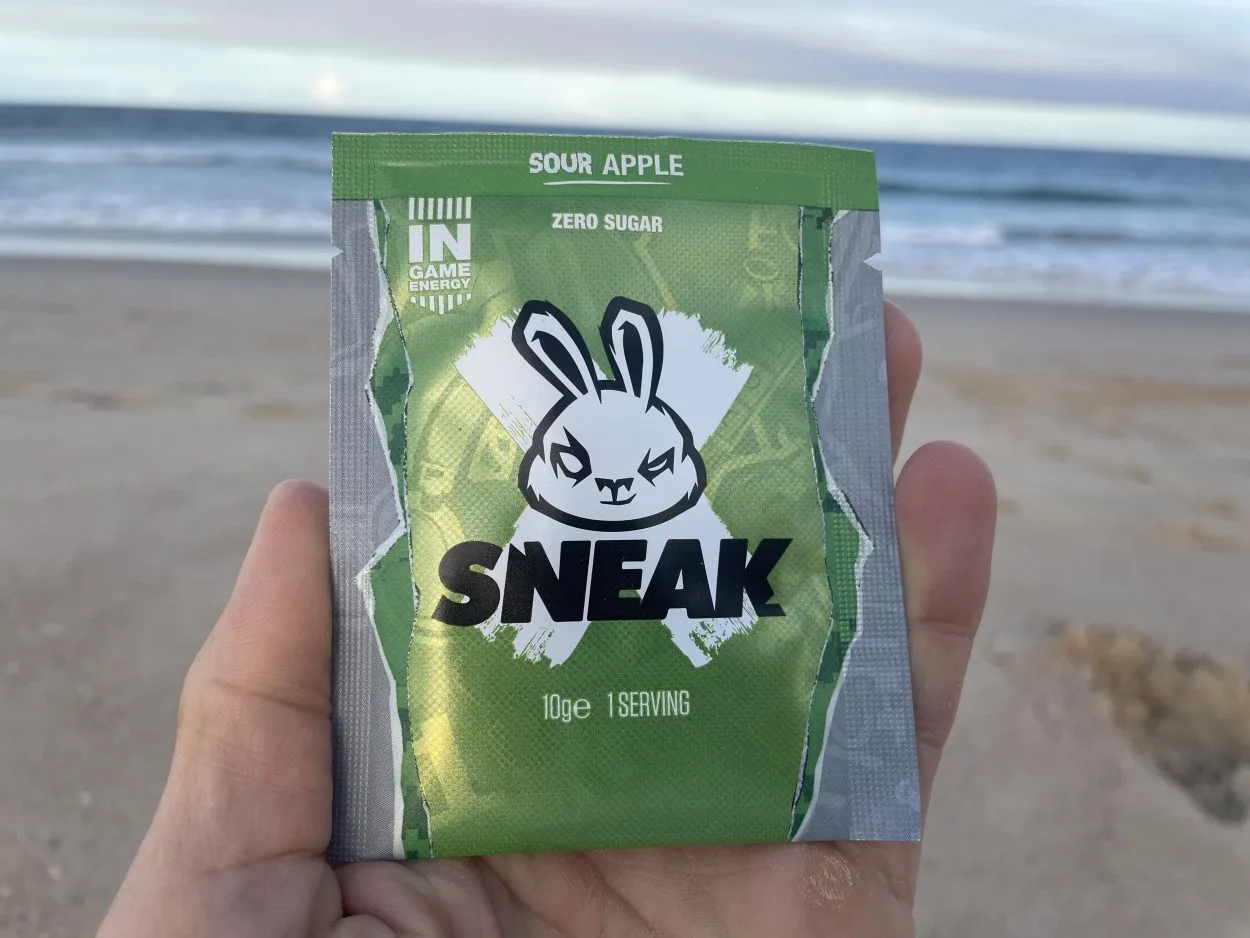 A person holding a sachet of Sneak Energy in Sour Apple flavor