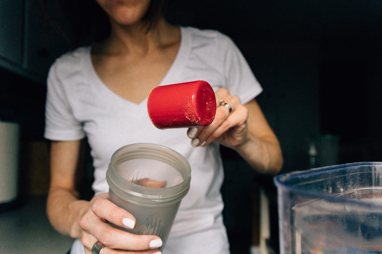 A woman in white t-shirt adding a scoop of powder in a blender