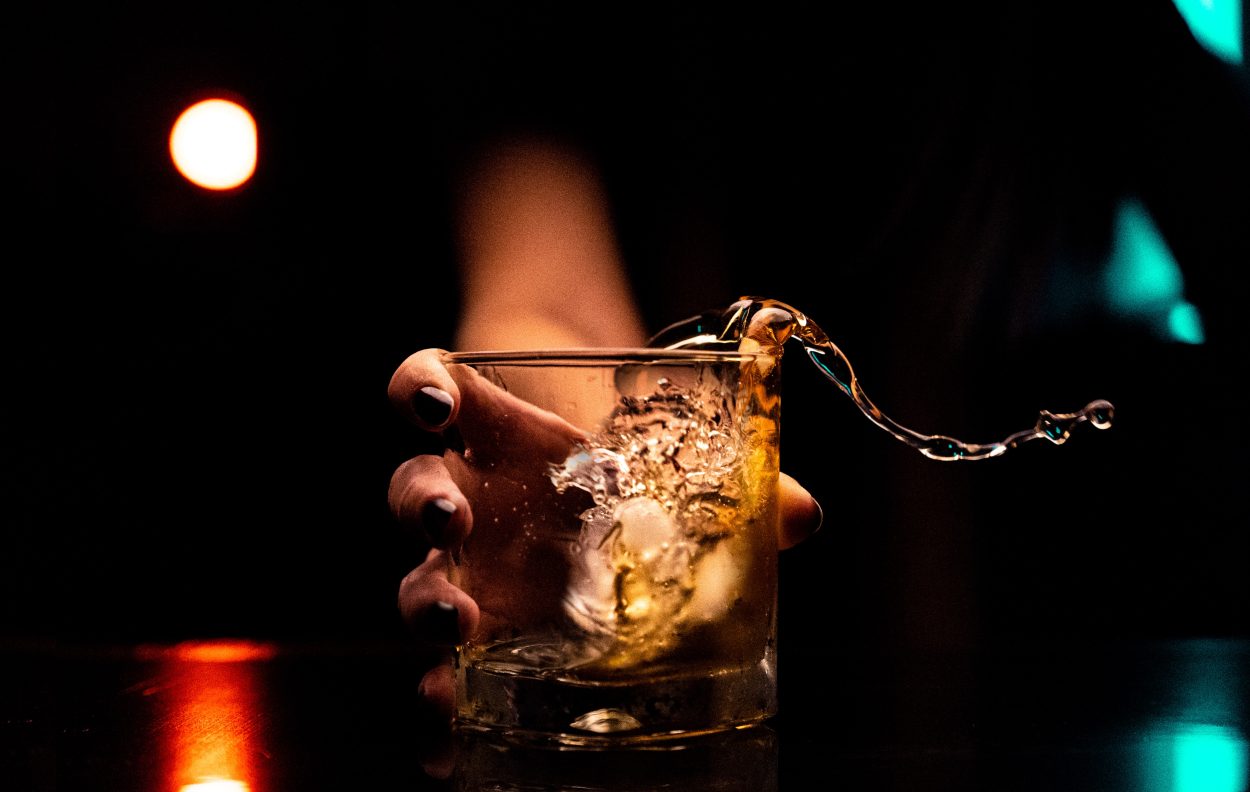 A women with black nail polish holding a glass with ice and alcohol