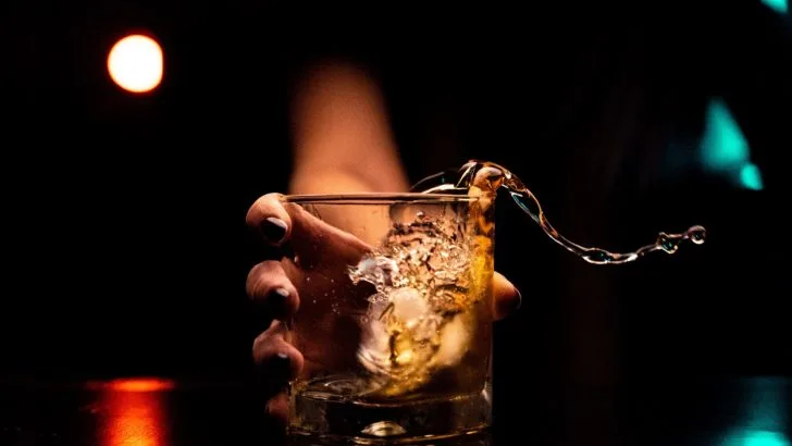 A woman with black nail polish holding a glass with ice and alcohol